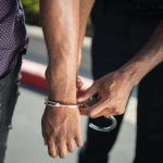 Close-up of a police officer handcuffing a suspect outdoors, enforcing law.