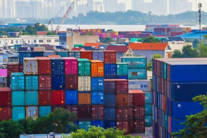 Vibrant stacked cargo containers at a bustling port with urban skyline in background.
