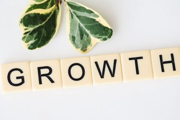 Close-up image of Scrabble tiles spelling 'Growth' with green leaves on a white background.