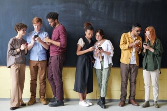 Young diverse adults using smartphones while standing against a blackboard, showcasing technology and connection.