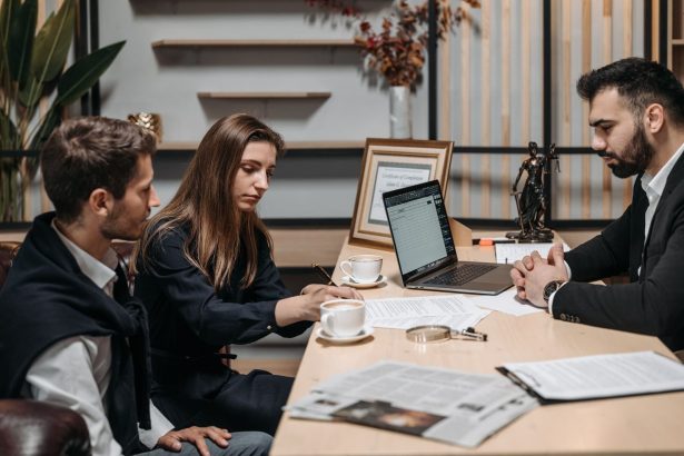 Three professionals discussing documents over coffee in a modern office setting.